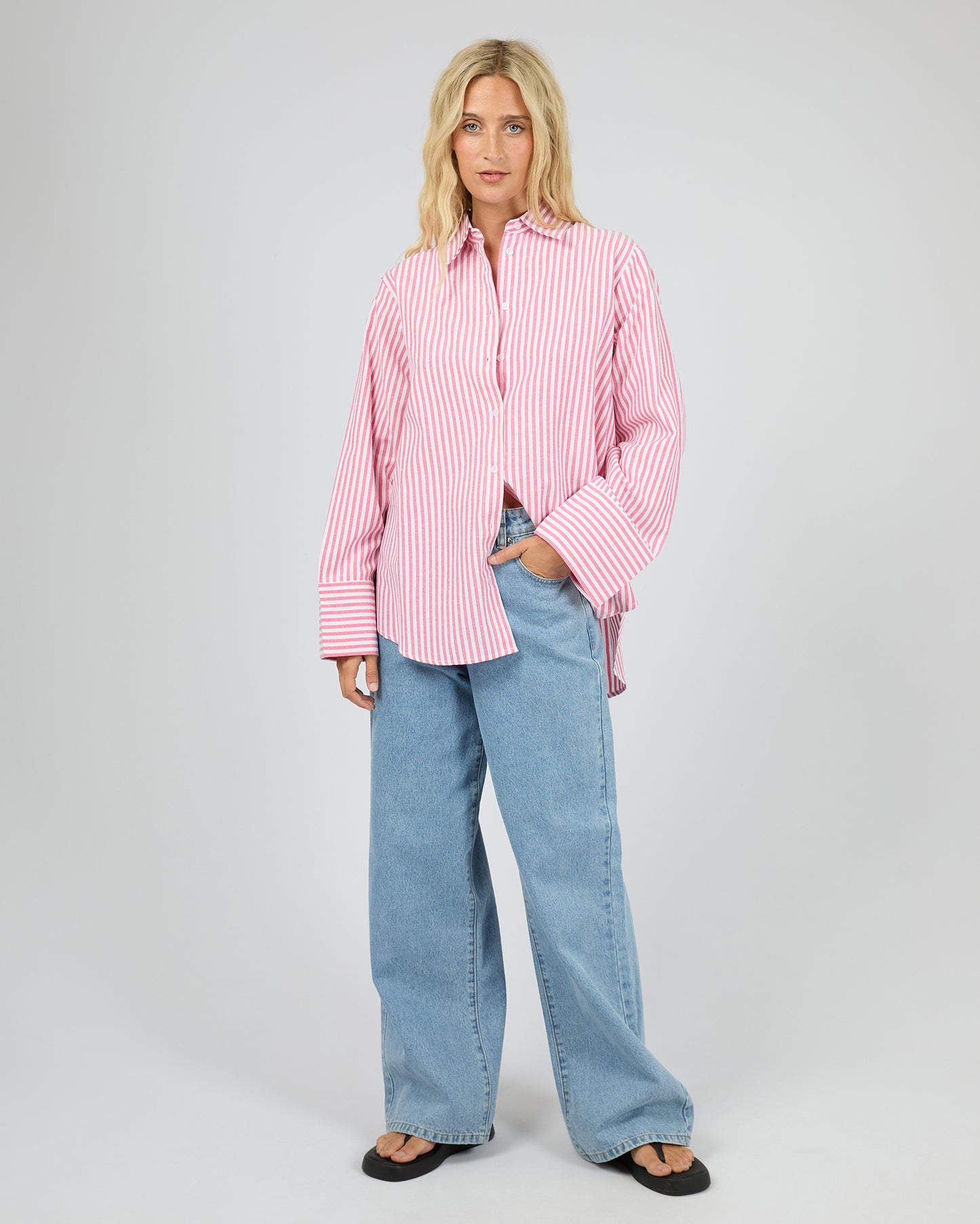Woman wearing a pink striped shirt and blue jeans on a gray background