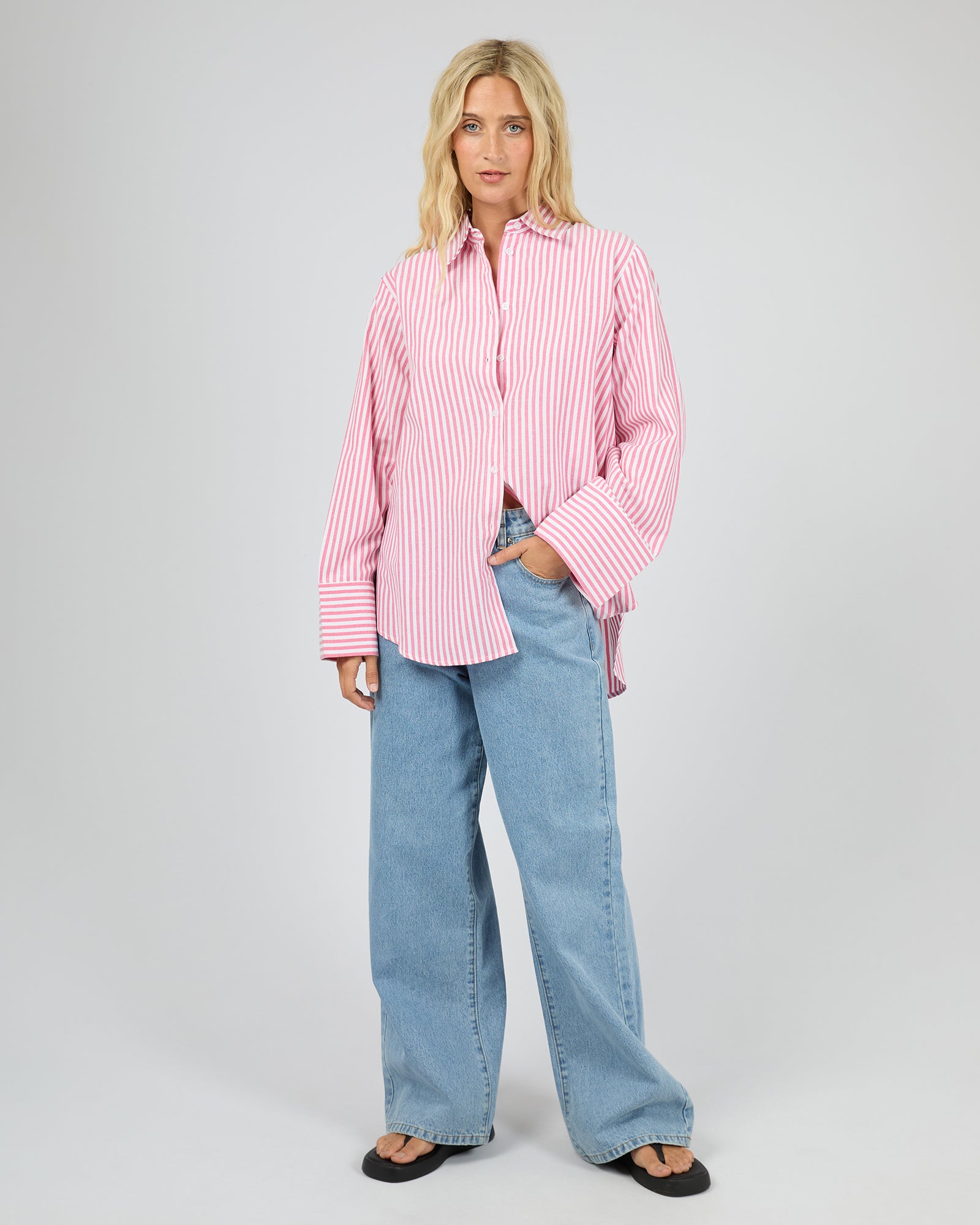 Woman wearing a pink striped shirt and blue jeans on a gray background