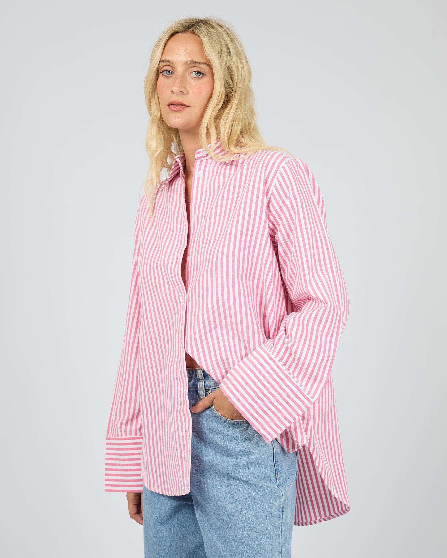 Person wearing a pink and white striped shirt with blue jeans on a plain background