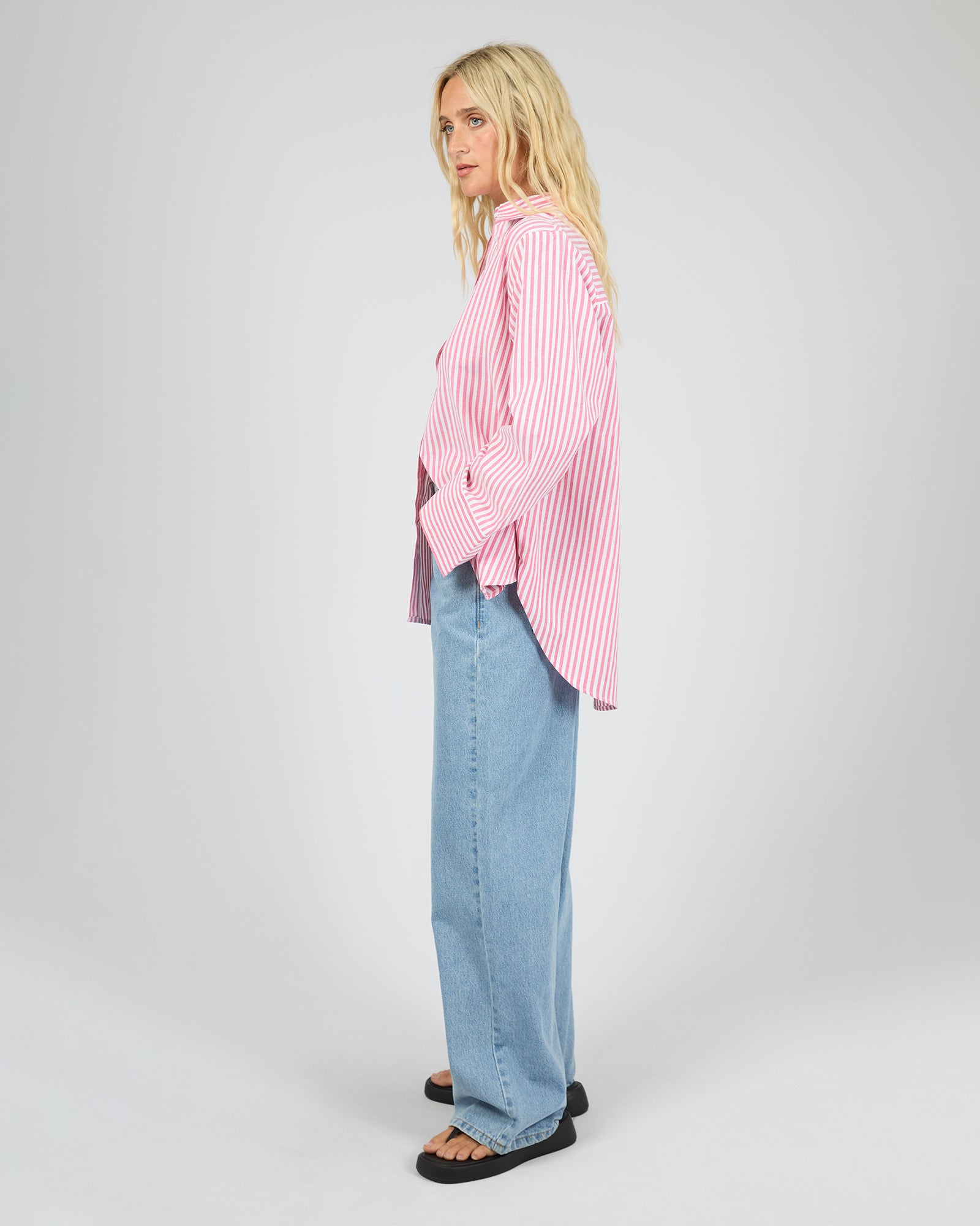 Person wearing a pink striped shirt and blue jeans on a white background