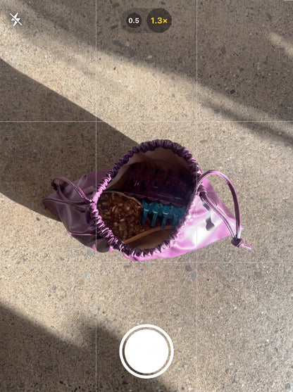 Purple drawstring bag with items on a concrete surface.Buttermilk Dev Bamboo Paddle Brush Toasted - The Rose Edit