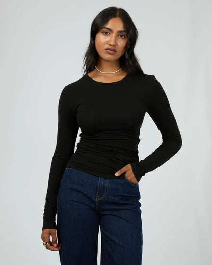 Woman wearing a black long-sleeve top and blue jeans against a plain background. Kylie Long Sleeve Top Black - The Rose Edit