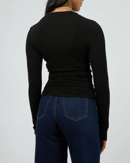Person wearing a black long-sleeve top and blue jeans on a plain background. Kylie Long Sleeve Top Black - The Rose Edit