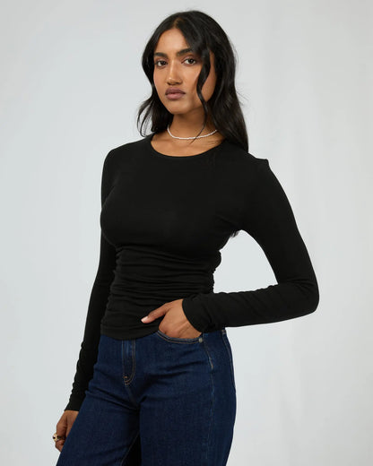 Woman wearing a black long-sleeve top and blue jeans against a plain background. Kylie Long Sleeve Top Black - The Rose Edit
