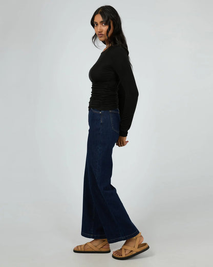 Woman wearing a black top and blue jeans on a white background. Kylie Long Sleeve Top Black - The Rose Edit
