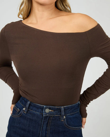 Person wearing a brown off-shoulder long-sleeve top and blue jeans on a plain background. Kylie Off Shoulder L/S Top Brown Close Up View - The Rose Edit