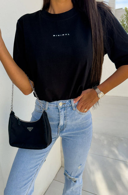 Person wearing a black t-shirt with 'MINIMAL' text, light blue jeans, and carrying a black handbag.