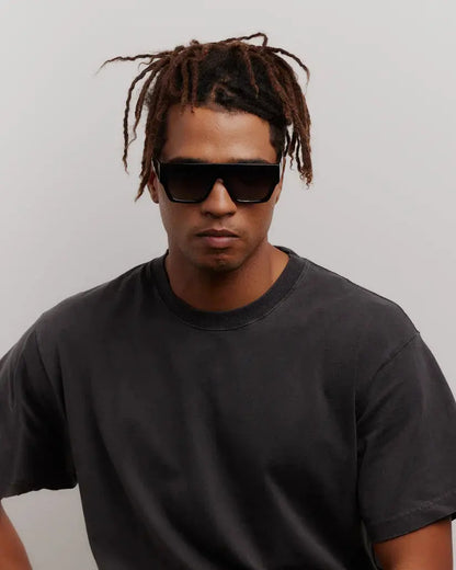 Man wearing black sunglasses and a black t-shirt against a plain background