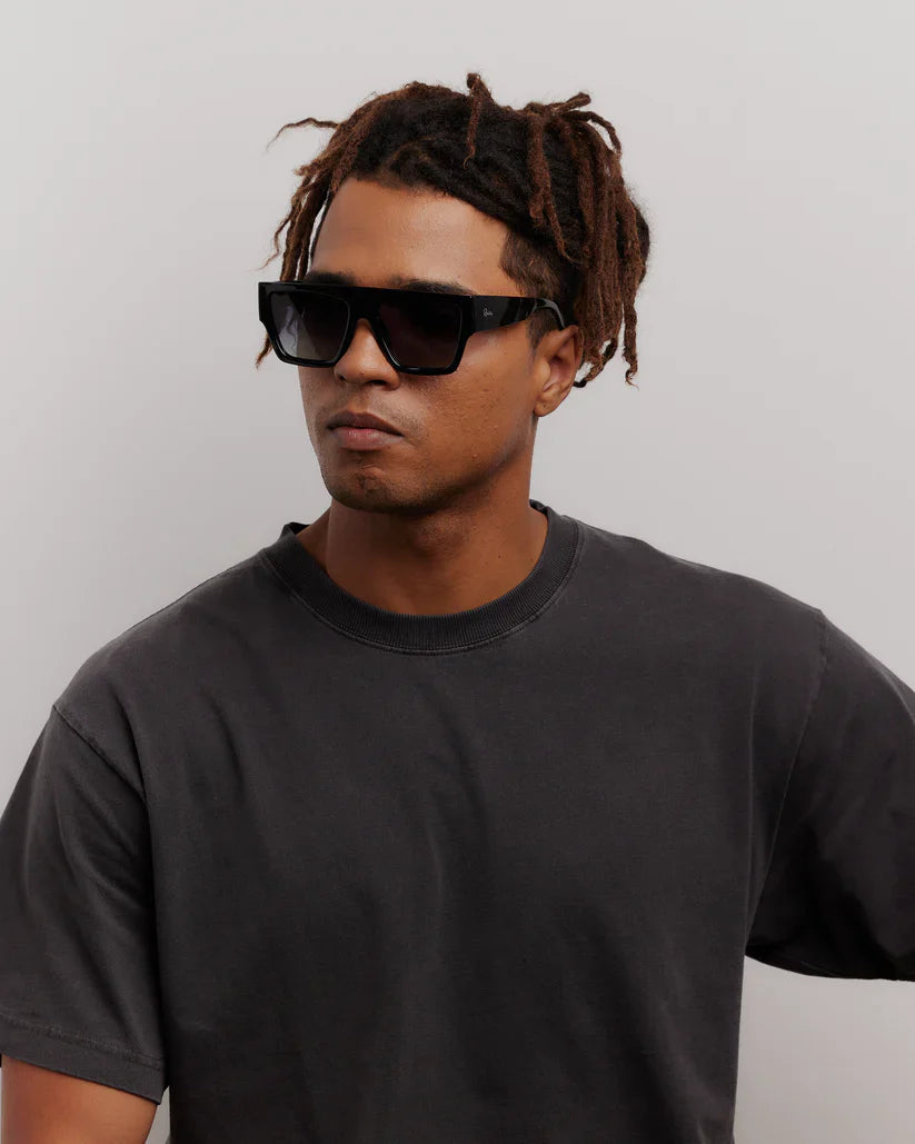 Man wearing black sunglasses and a black t-shirt against a plain background