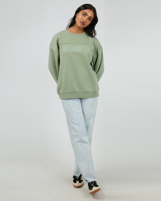 Person wearing a green sweatshirt and light blue jeans on a white background