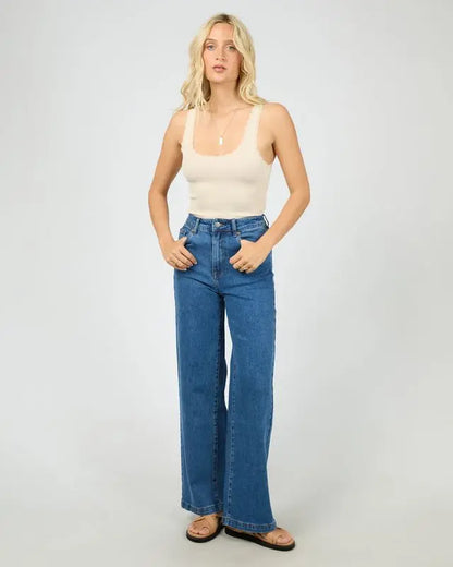 Woman wearing a white tank top and blue jeans on a plain background. Washed Rib Lace Tank Vanilla - The Rose Edit