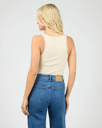 Woman wearing a beige tank top and blue jeans on a white background. Washed Rib Lace Tank Vanilla - The Rose Edit
